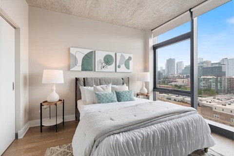 A bedroom with a large bed and a city view through the window.