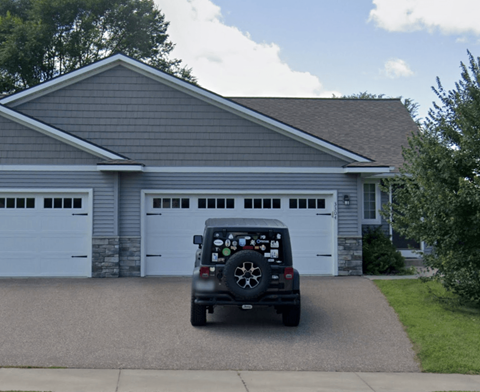 A black jeep is parked in front of a house with two garages.
