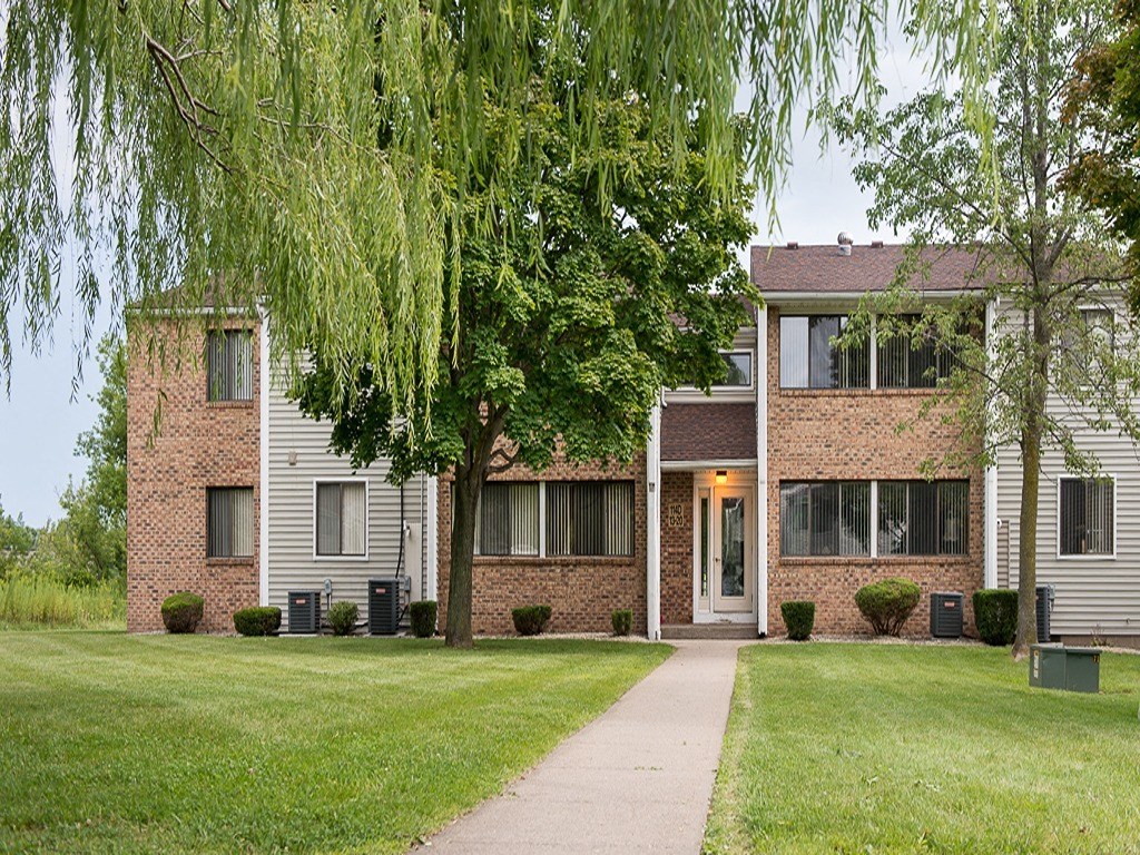 an apartment building with a sidewalk and trees in front of it