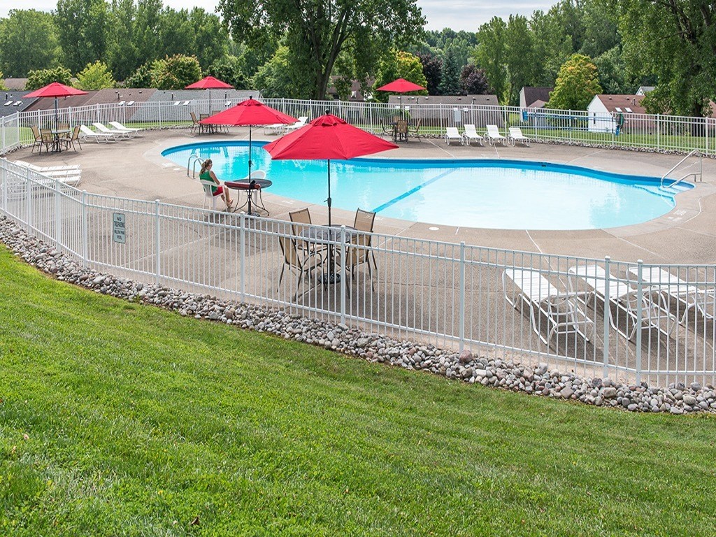 a swimming pool with tables and umbrellas behind a metal fence