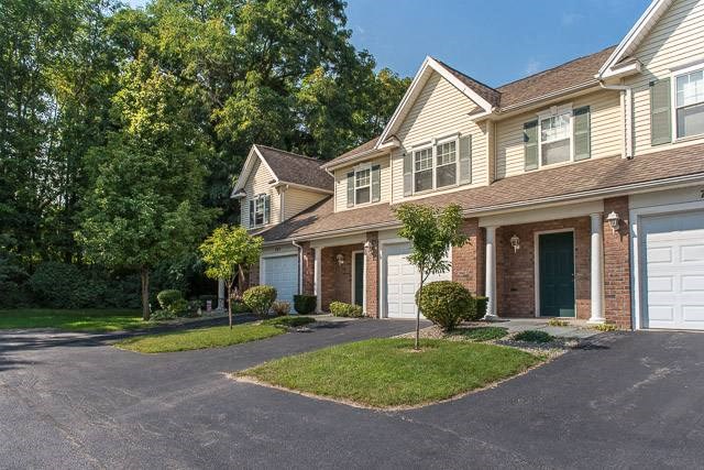 Exterior view of 2-story townhomes with private covered entrances & attached 1-car garages near woods