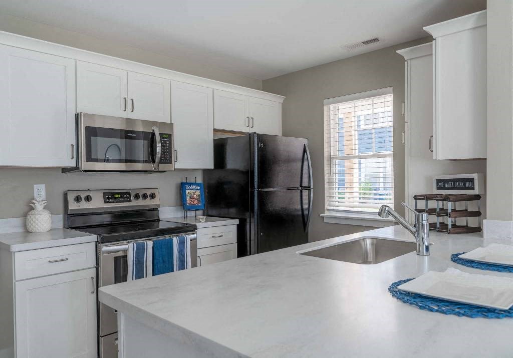 View of modern kitchen area with white shaker-style cabinetry, stainless steel appliances, and kitchen break bar