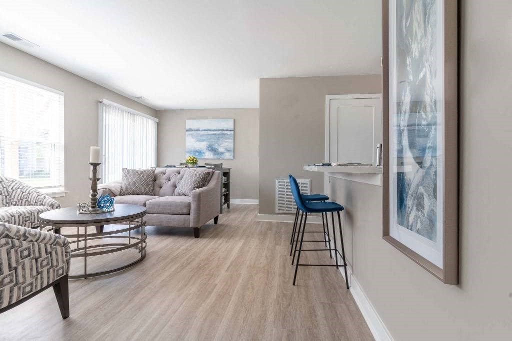 View of great room from the foyer showing living area seating, kitchen breakfast bar, large windows, dining room table ar the far end and sliding glass doors to the private patio or balcony