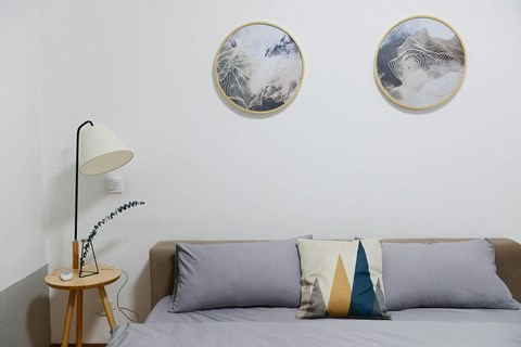 A bedroom with a grey bed and two round pictures on the wall.