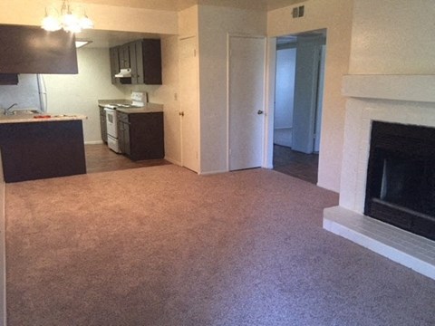 an empty living room with a fireplace and a kitchen