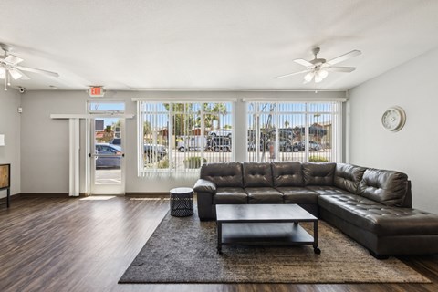 A black leather couch sits in a living room with a ceiling fan and a large window.