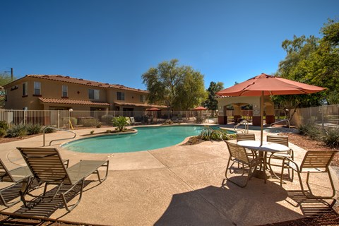 A pool with chairs and a table in front of a house.