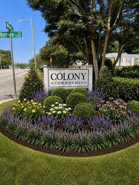 A sign for Colony Townhomes is surrounded by a flower bed.