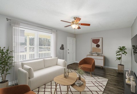 A living room with a white couch, a brown chair, a coffee table, and a ceiling fan.