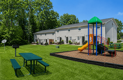A playground with a green slide and a picnic table in front of a grey building.