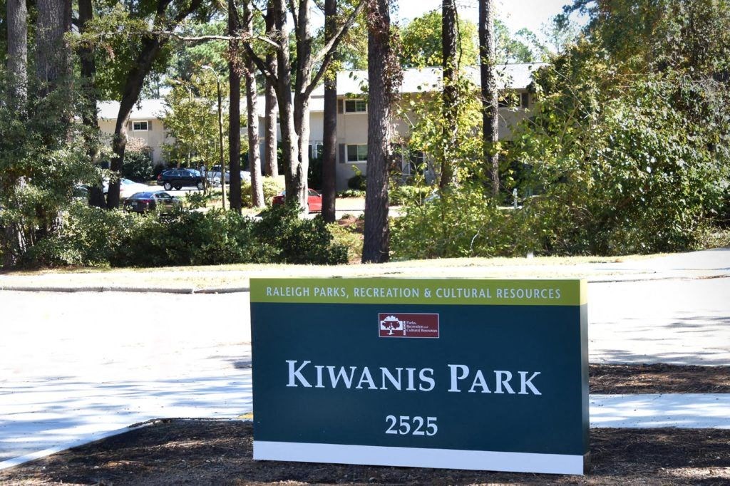 a sign for kiwis park in front of trees