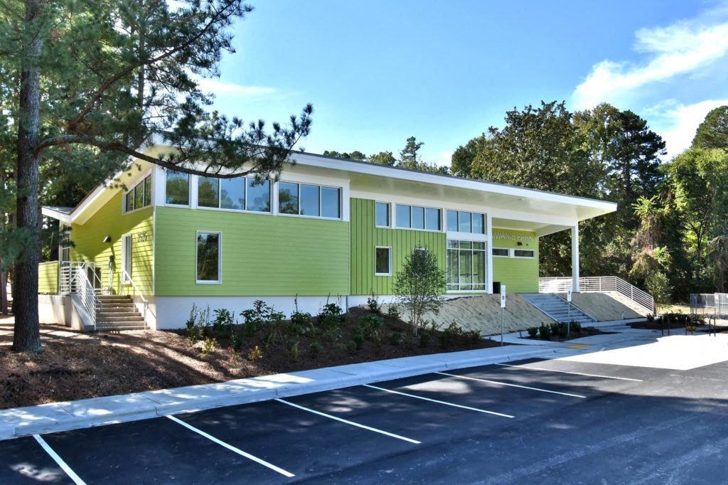 the front of a green house with trees and a parking lot