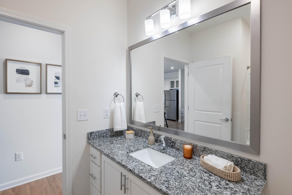 A bathroom with a granite countertop and a large mirror.at Evolve at Parkway Apartment Homes, Concord, 28027