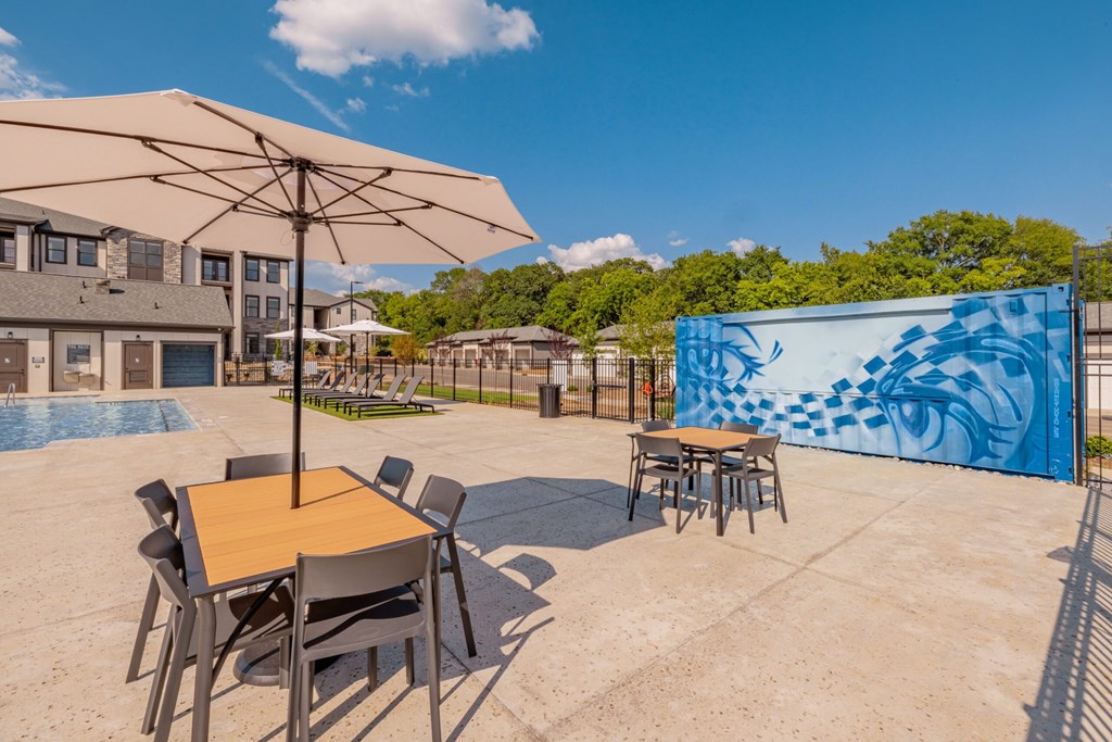 A table with chairs and an umbrella is in the foreground of a patio area.at Evolve at Parkway Apartment Homes, Concord