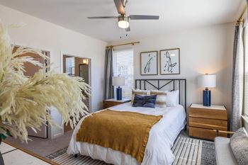 A bedroom with a bed, a ceiling fan, and a nightstand with a lamp.