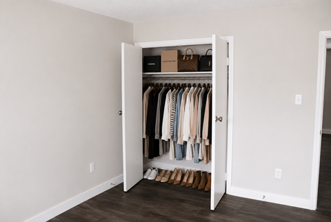 A white closet with clothes hanging and a box on the shelf.