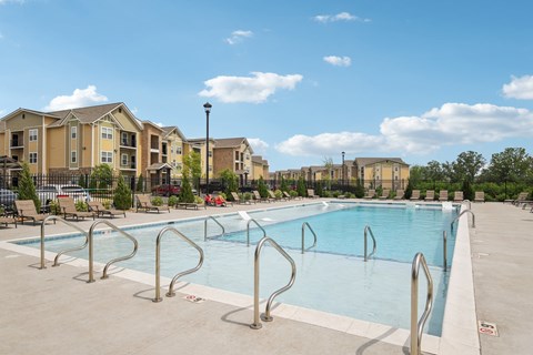 A large swimming pool surrounded by a metal railing and apartment buildings in the background.
