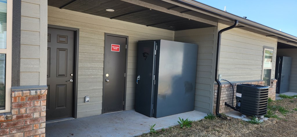 A black storm shelter is outside a house.