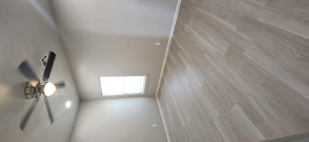 A ceiling fan is mounted on the wall in a room with light wood flooring and a skylight.