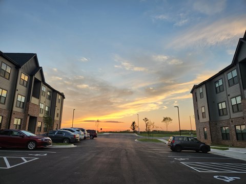 A parking lot with cars parked and buildings on either side during sunset.