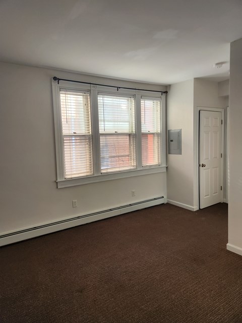 A room with brown carpet and a window with blinds.