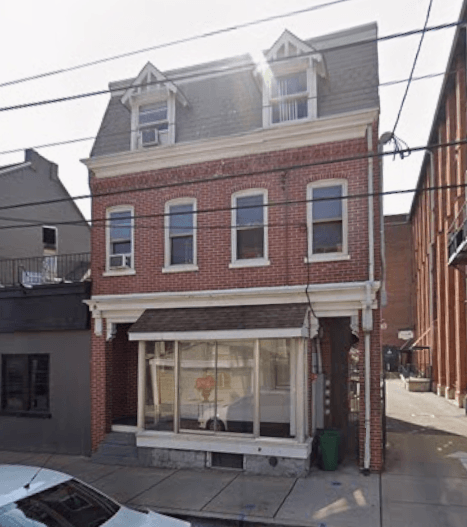A red brick building with a white trim and a black car parked in front.