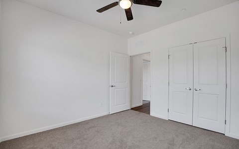 A room with a ceiling fan and three doors.