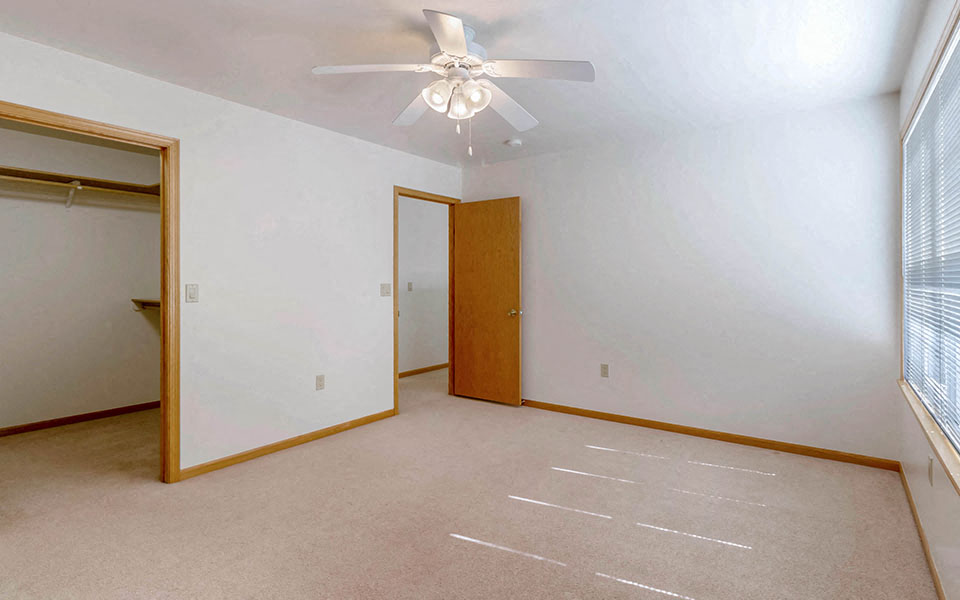 an empty bedroom with a ceiling fan and a closet