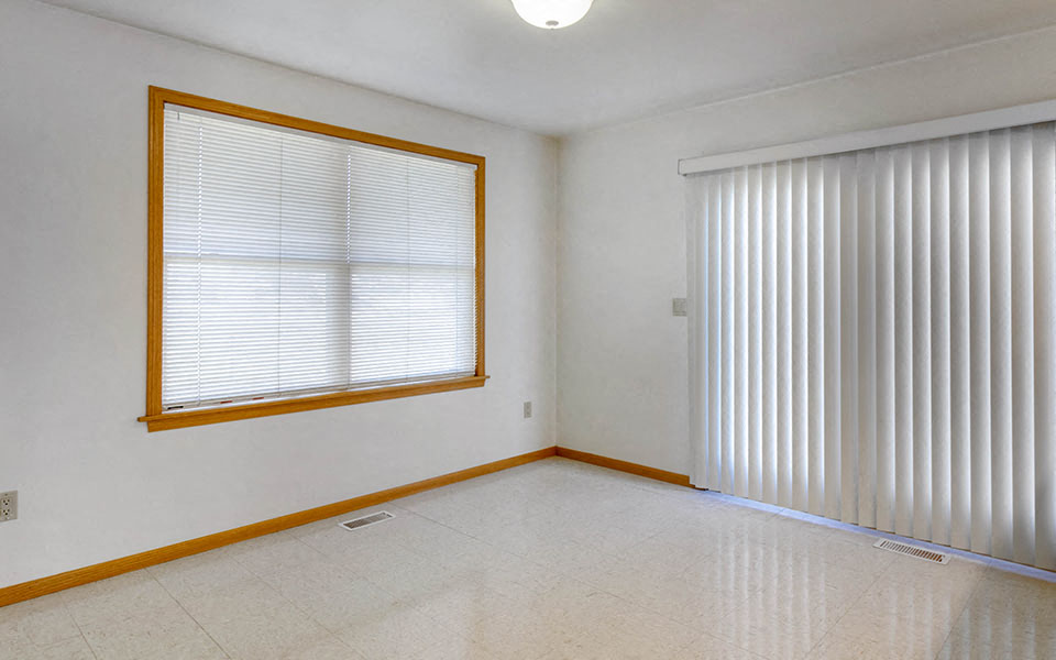 an empty living room with a large window and white blinds