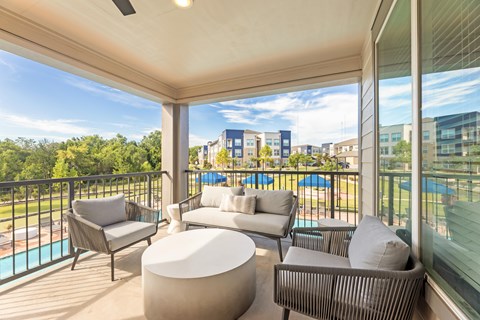 A balcony with a white couch, grey armchair, and a white ottoman at The Preserve at Preston Trails Apartments, Cedar Hill, TX, 75104
