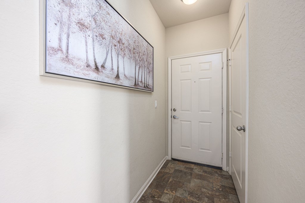 A hallway with a picture of trees on the wall and a white door.
