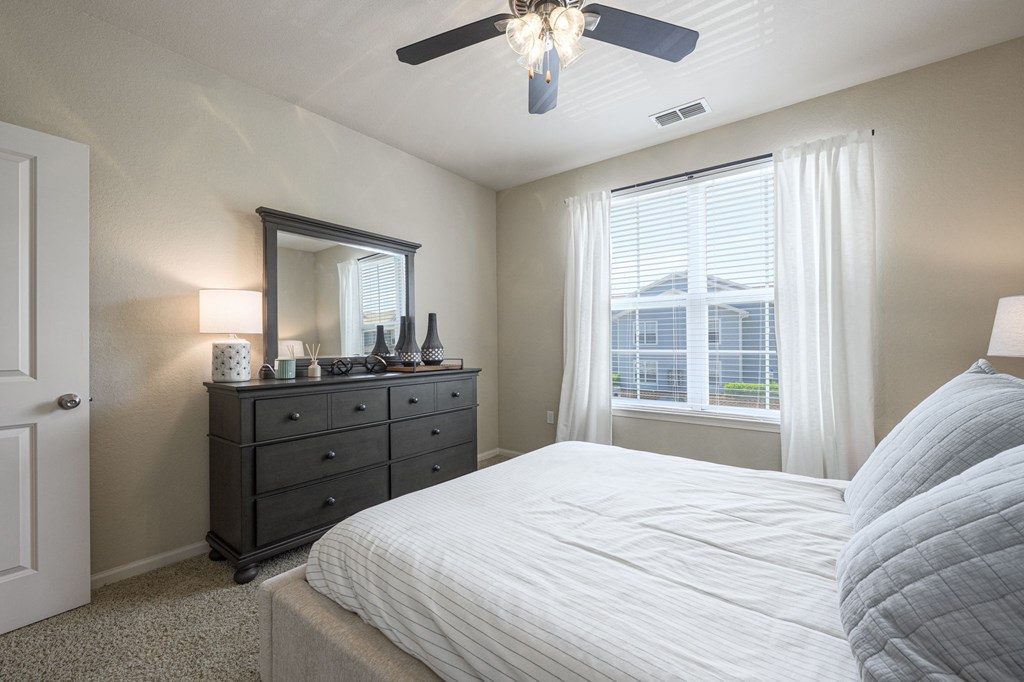 A bedroom with a large bed, a dresser with a mirror, and a ceiling fan.