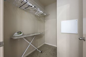 A white ironing board with clothes hangers on the wall.