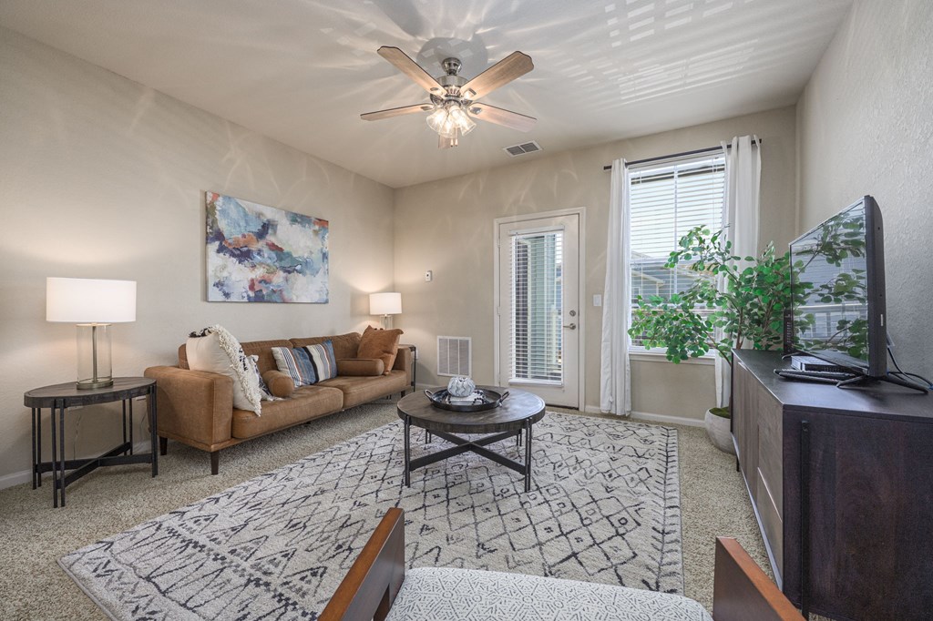 A living room with a brown couch, a coffee table, and a ceiling fan.