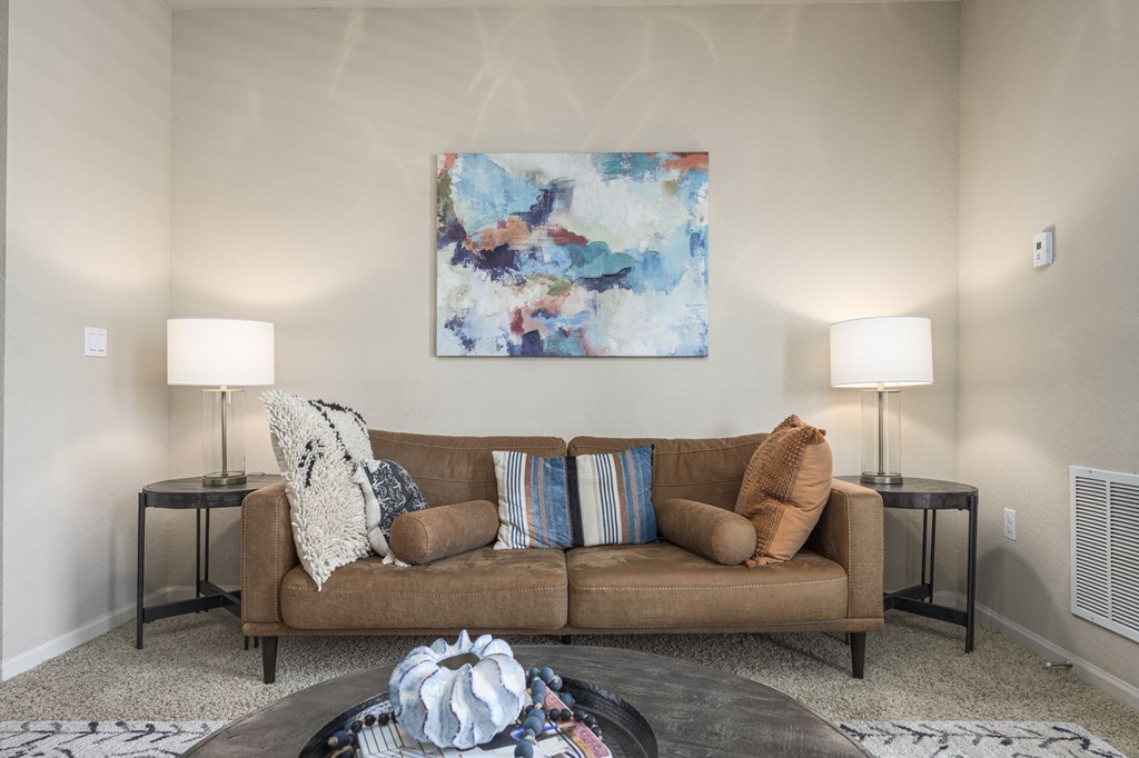 A living room with a brown couch, a painting on the wall, and two lamps on either side.