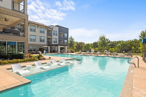 A large swimming pool with lounge chairs and apartment buildings in the background at The Preserve at Preston Trails Apartments, Cedar Hill