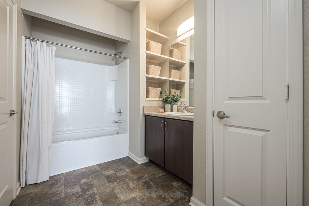 A bathroom with a tub, sink, and a cabinet with shelves.