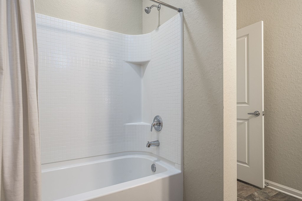 A white bathtub with a shower head and a curtain.