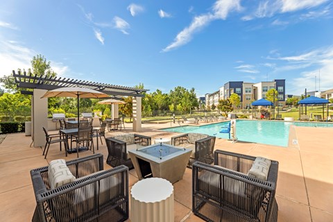A poolside area with chairs and a table at The Preserve at Preston Trails Apartments, Texas, 75104