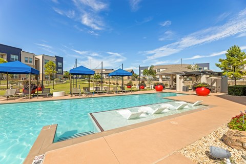 A swimming pool with a glass divider in the middle and a blue umbrella on the left at The Preserve at Preston Trails Apartments, Cedar Hill, Texas