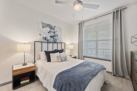 A bedroom with a bed, two lamps, and a painting on the wall at The Preserve at Preston Trails Apartments, Cedar Hill, TX, 75104