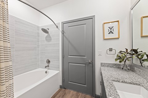 A bathroom with a white tub, grey door and a plant at The Preserve at Preston Trails Apartments, Cedar Hill