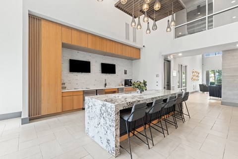 A modern kitchen with a marble island and black chairs at The Preserve at Preston Trails Apartments, Texas