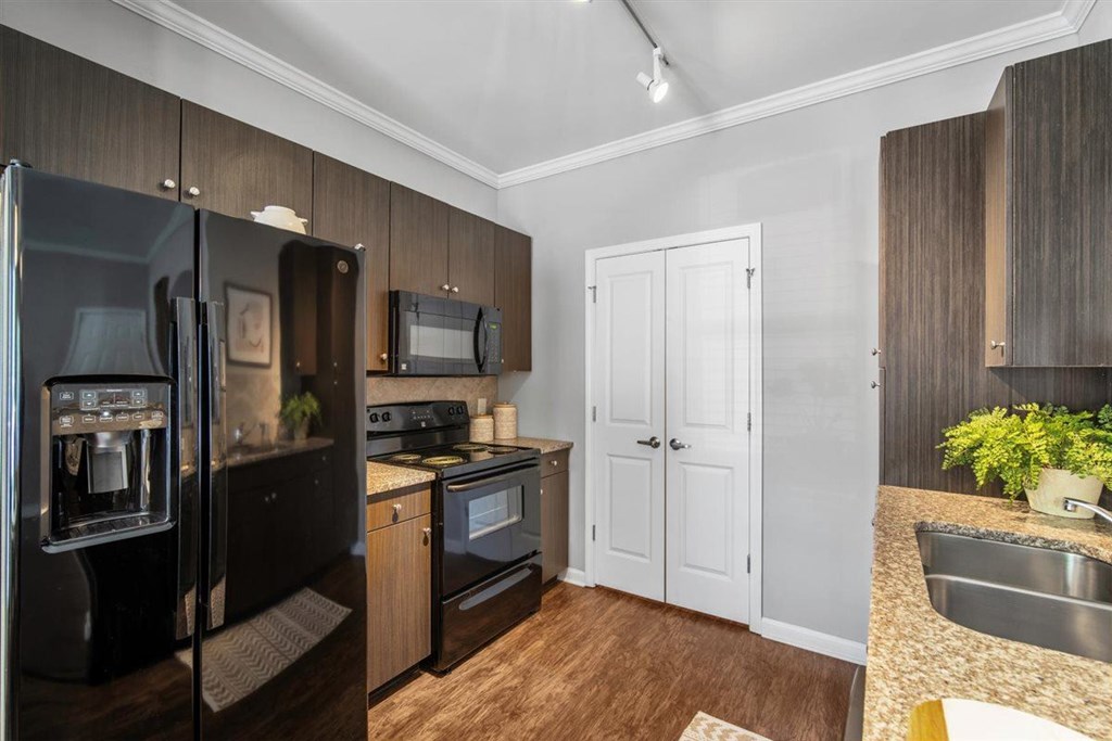 A kitchen with a black fridge, white cabinets, and a wooden floor. at Cypress River, Ladson, 29456