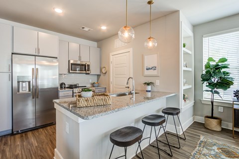 A kitchen with a refrigerator, bar stools, and a potted plant.