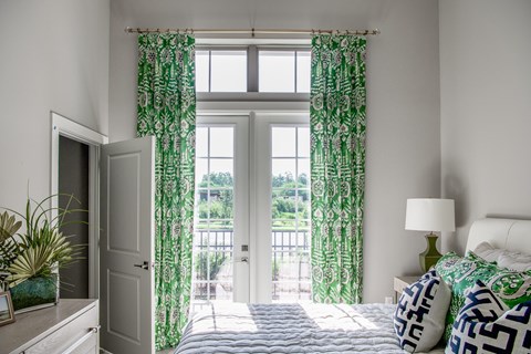 A bedroom with a bed, nightstand, and window with green curtains.
