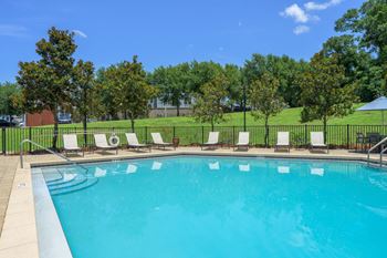 A pool surrounded by trees and chairs.