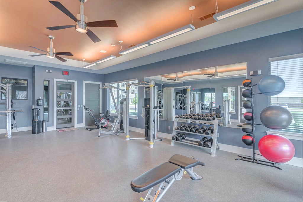 A spacious gym with a variety of equipment including weights, a bench, and a ball.