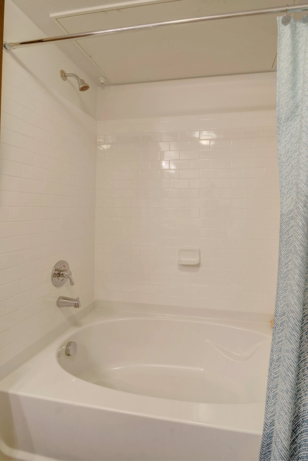 A white bathtub with a shower head and a blue shower curtain.
