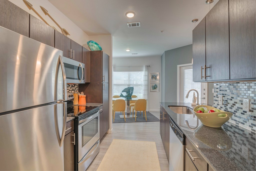 A modern kitchen with stainless steel appliances and a dining area with chairs.